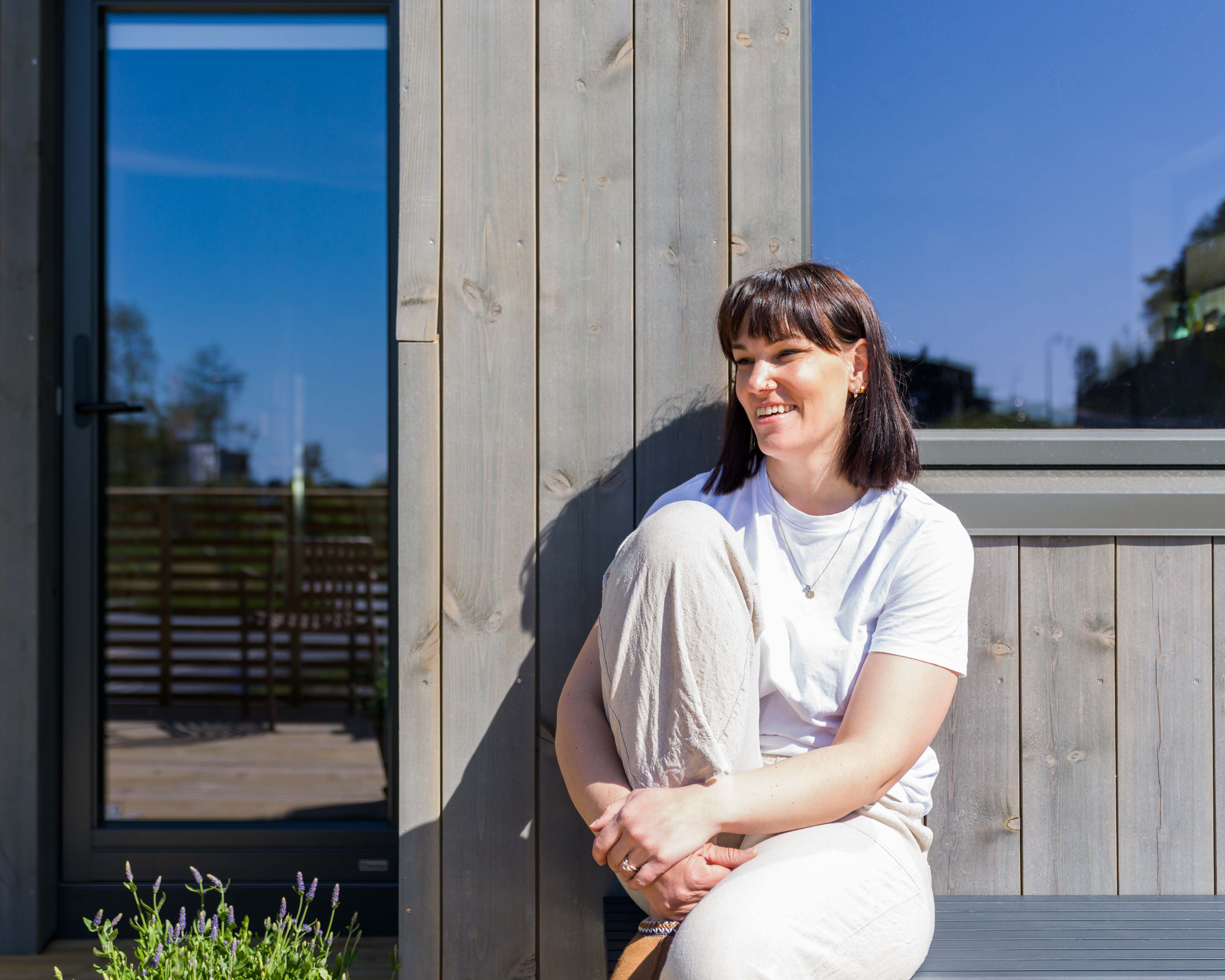 Huseier Helene på benk foran huset sitt med Moelven Værbitt kledning i fargen Gråna.