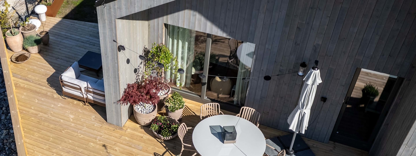 Et grått hus med parasoll, terrasse, planter og møbler