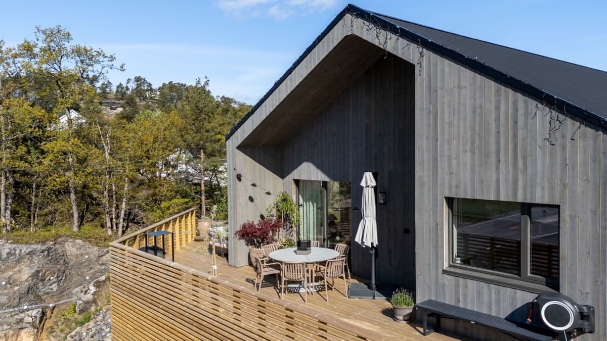 Rundt spisebord med flere stoler på romslig terrasse, omgitt av krukker, utemøbler og moderne fasade.