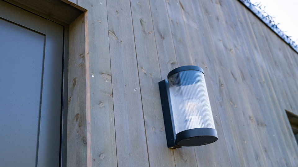 En grå husvegg med dør og en lampe i sort metall