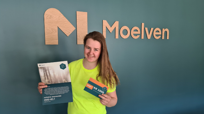 HMS-hjälten Kathrin Svehaugen i gul tröja håller upp ett diplom och presentkort