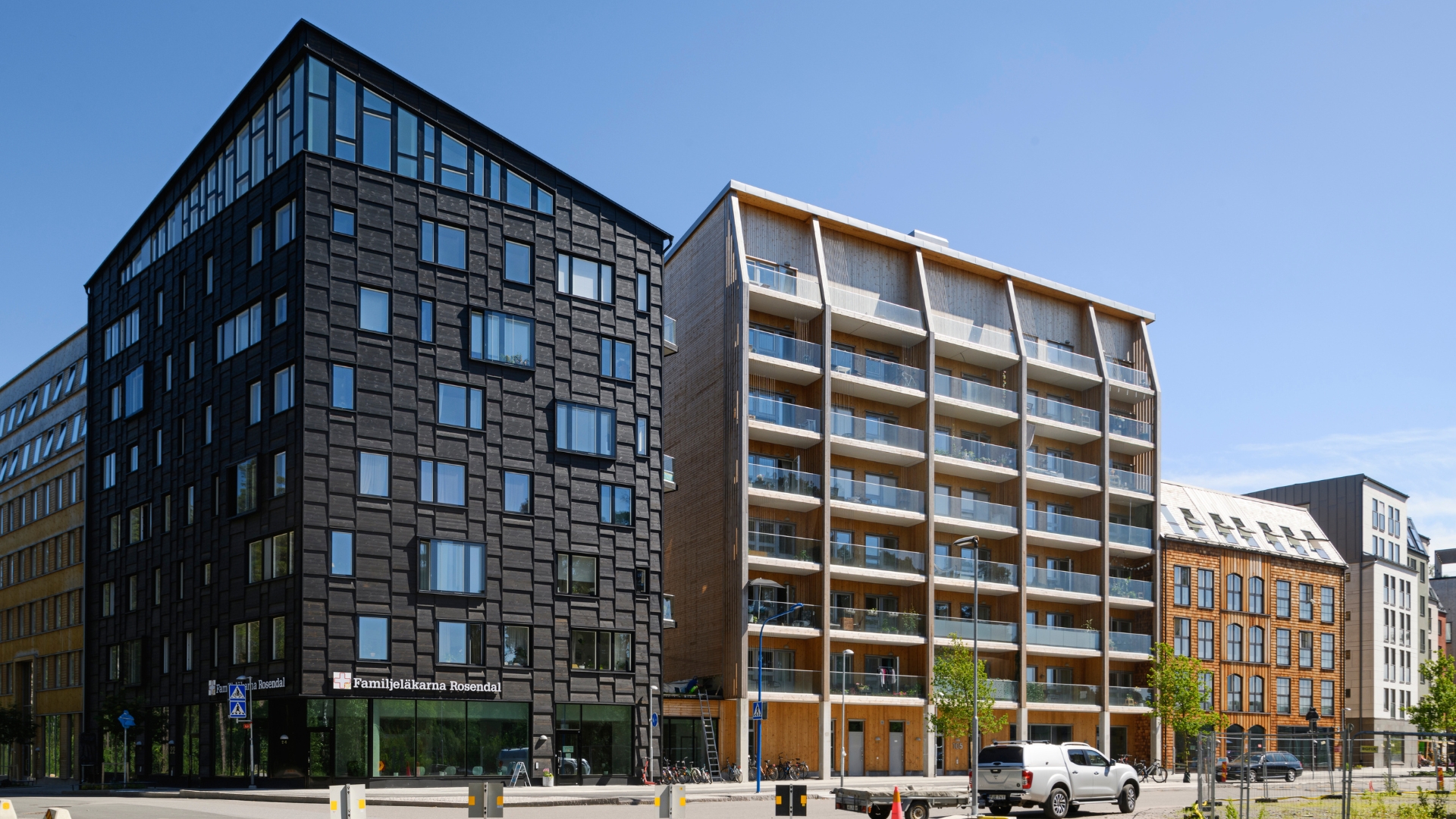 Stora byggnader med många fönster i olika träfasader, blå himmel