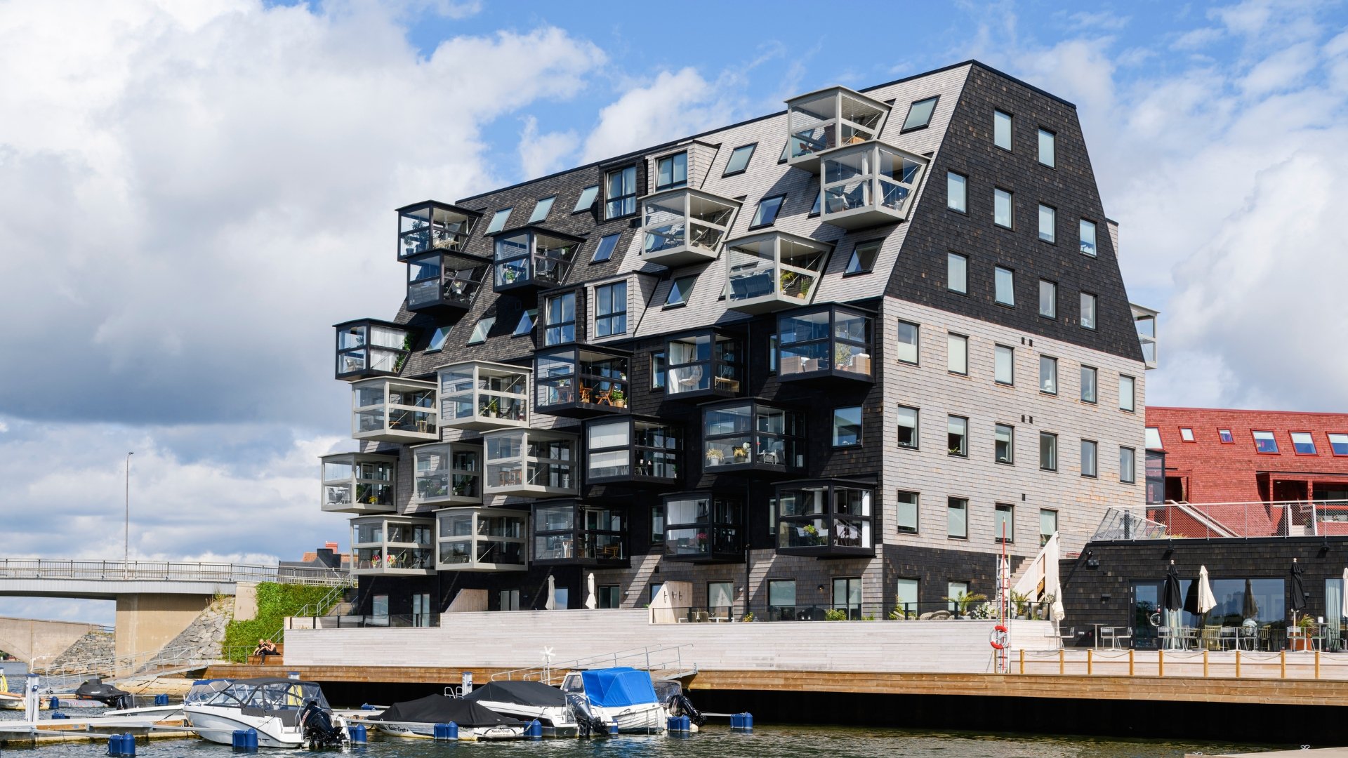 Stor byggnad vid vattnet med träfasad i grå och svarta toner. båt på vattnet.