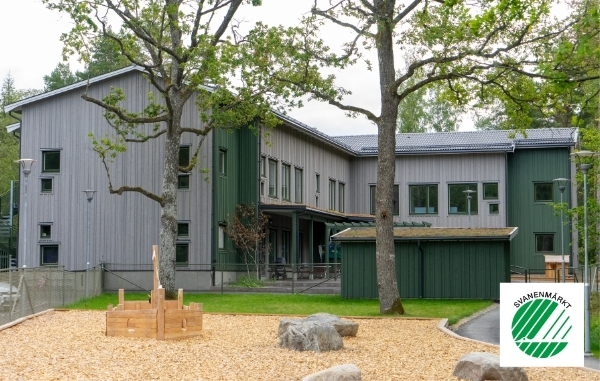 Förskola i grått och grönmålad trä med lekplats framför