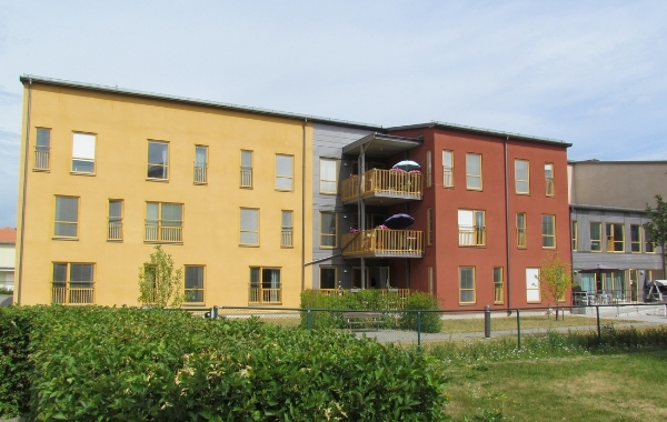 Omsorgsboende fotad från utsidan. Gul och rödmålad fasad. Grönområde utanför byggnaden.