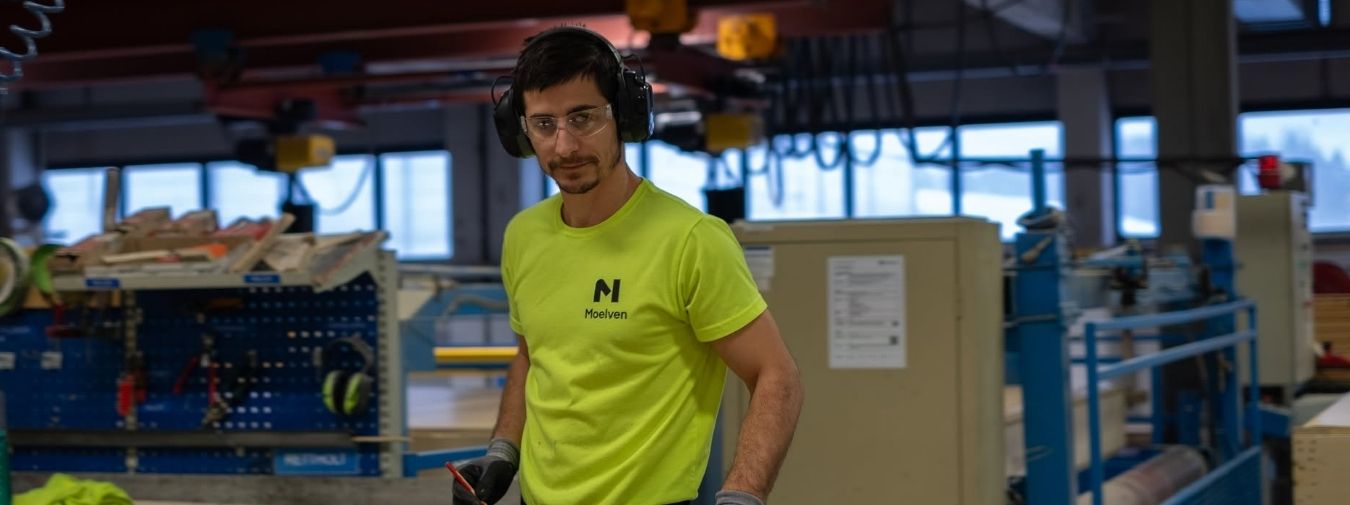 En produksjonsarbeider med hørselvern inne i et fabrikklokale