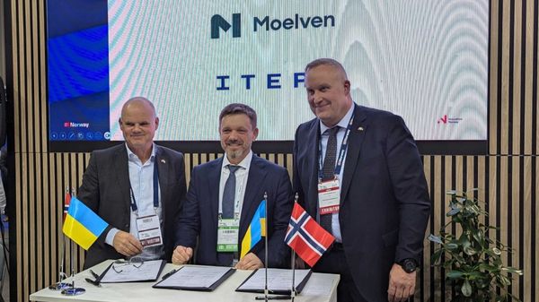 Tre dresskledde og smilende menn har signert avtaler. Norske og ukrainske flagg på bordet.