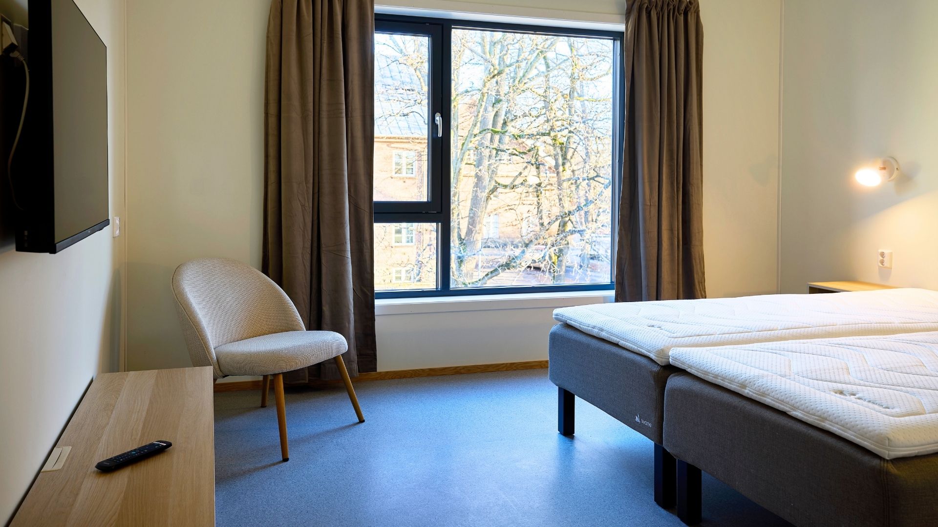 Hotellrom med dobbeltseng, TV og TV-benk. Stort vindu slipper inn masse lys.