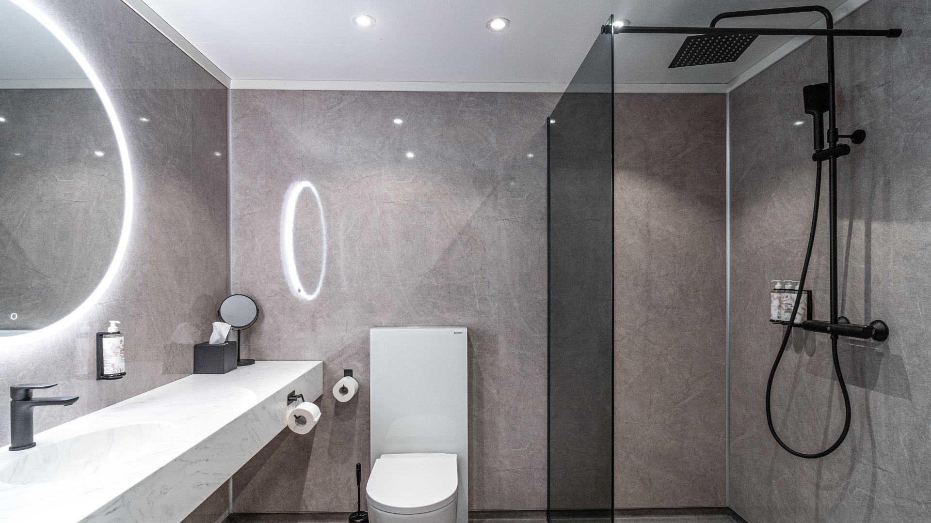 Bad med grå vegger, speil, dusj og WC.