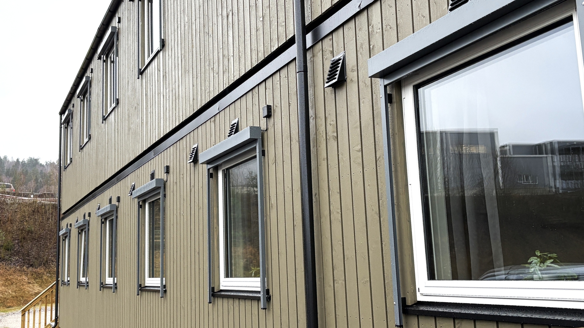 Udvendig facade på boligpavillon i to etager med vinduer og træbeklædning.