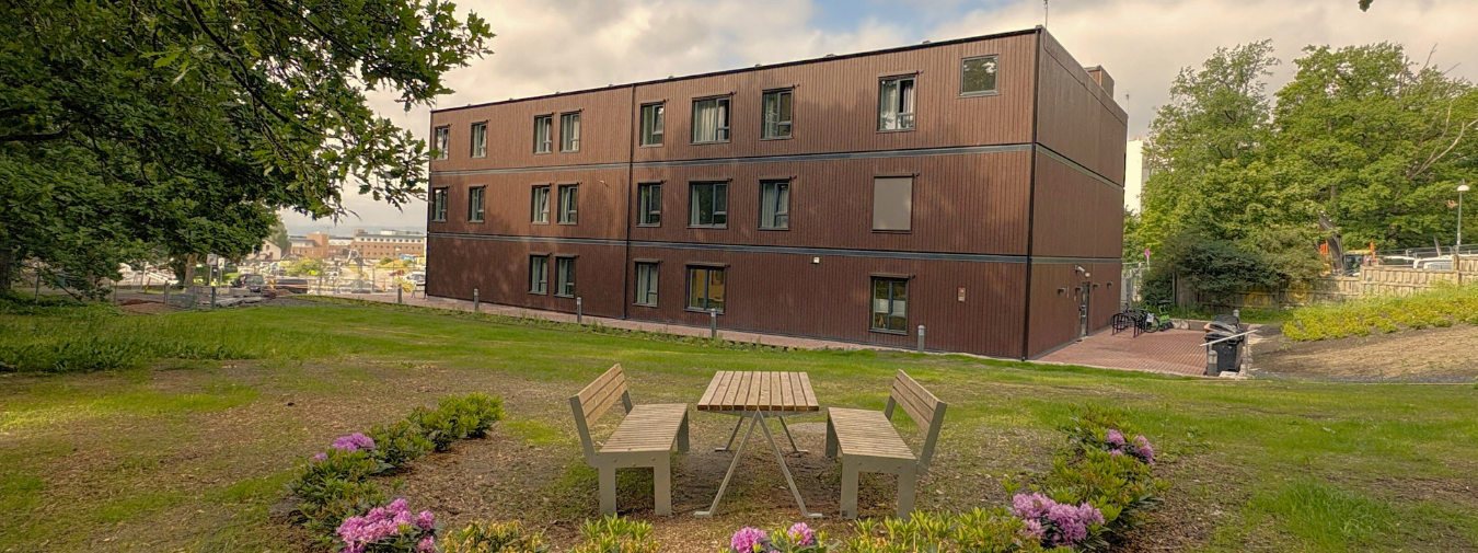 Three-story modular wooden building in Oslo. Planting and seating area in front.