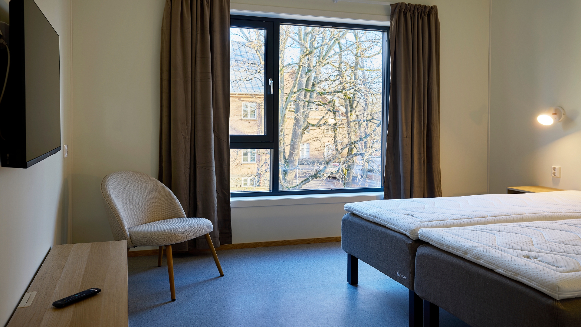 Hotel room with a double bed, TV bench and a view towards the window.