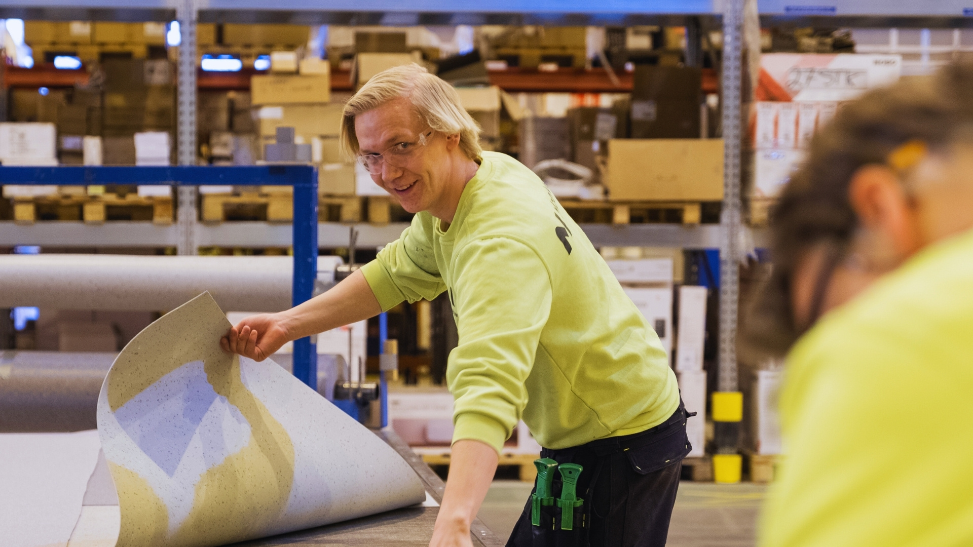 Factory worker holding flooring material and smiling at the camera.