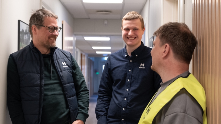 Three smiling Moelven colleagues are standing in a corridor.