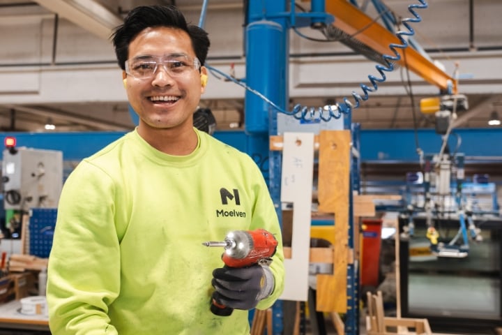 Smiling factory worker holding a nail gun.