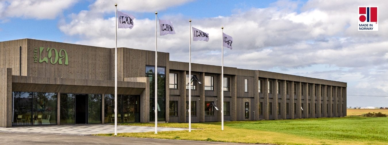 Three-story modular wooden building in Oslo. Planting and seating area in front.