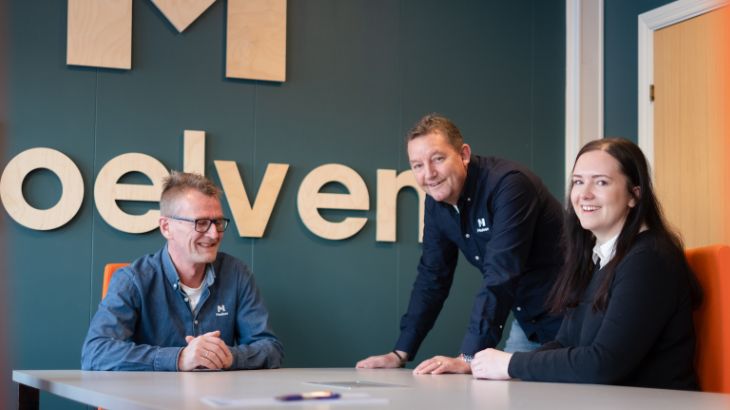 Þrír brosandi Moelven-samstarfsmenn við borð.