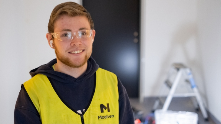 Ung, smilende person med Moelven refleksvest og vernebriller.