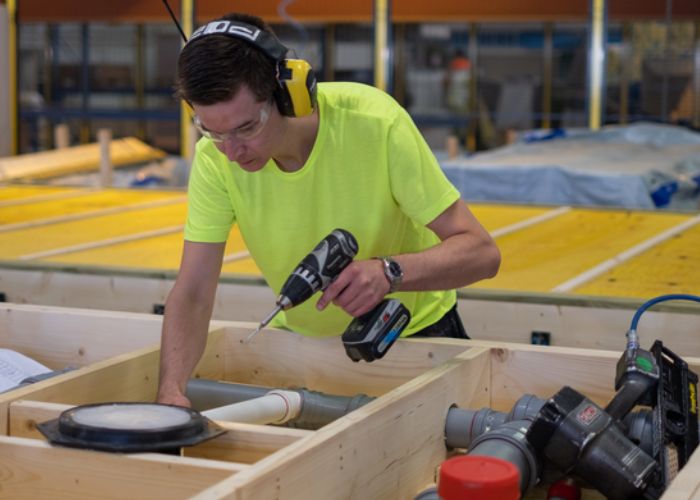 Person som bruker en drill i en trekonstruksjon i Moelven Byggmodul sin fabrikk.