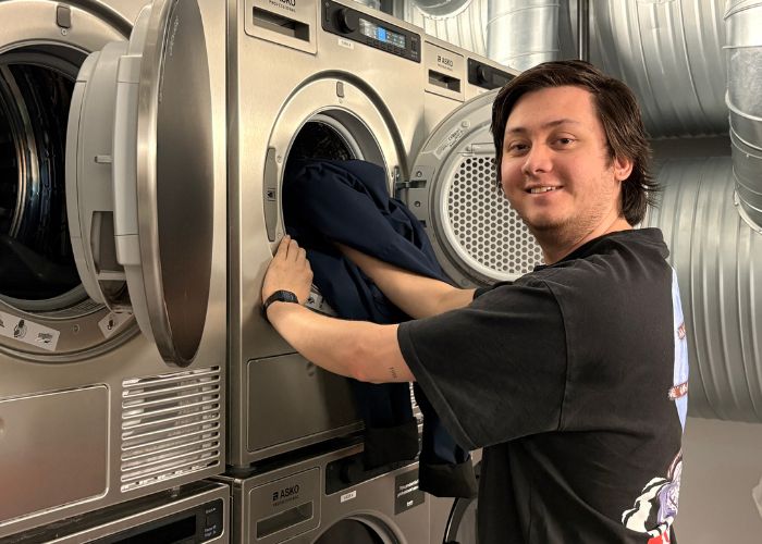 Person som putter klær inn i en vaskemaskin.