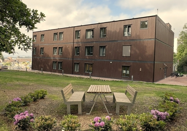 Treetasjes modulbygg med beplantning og sittegruppe utenfor.