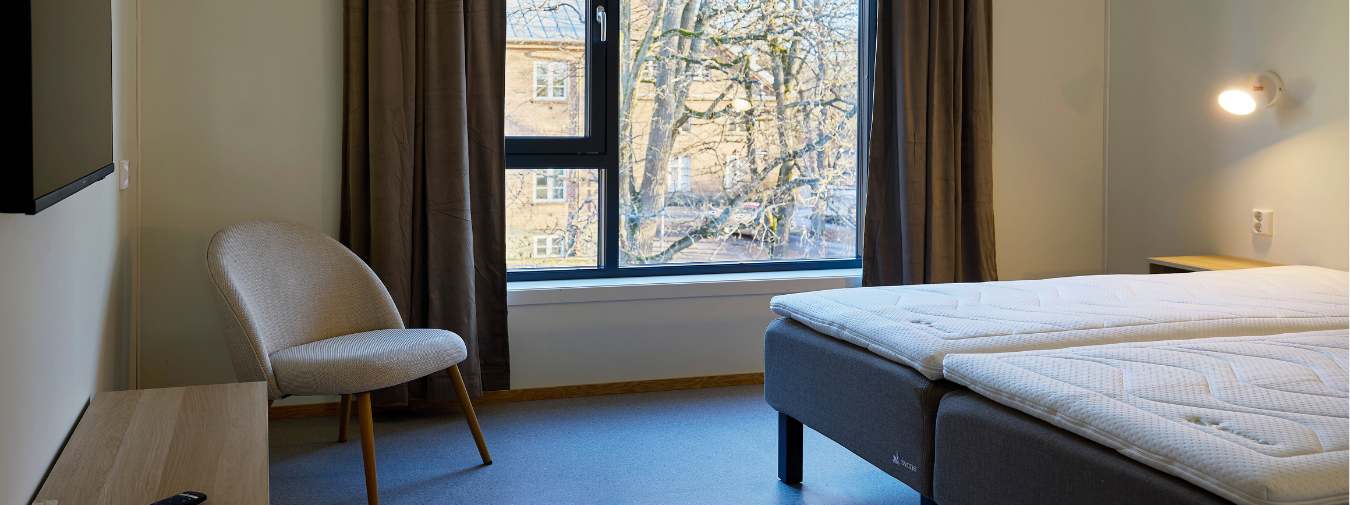 Møblert hotellrom med stort vindu, dobbeltseng og møbler.
