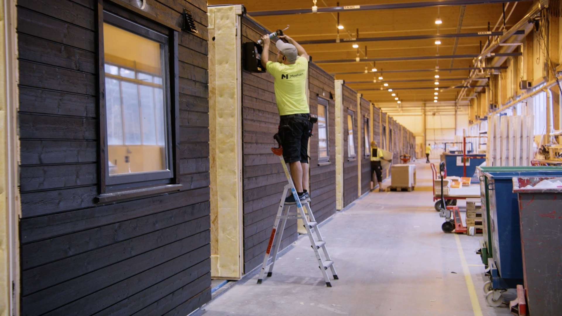 Full fart i fabrikken til Moelven Byggmodul AS, person som jobber på modul med mørk kledning