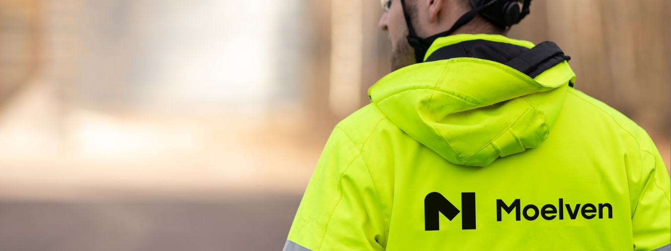 Person med synlighetsjakke og Moelven-logo på ryggen. Han har hjelm på hodet.