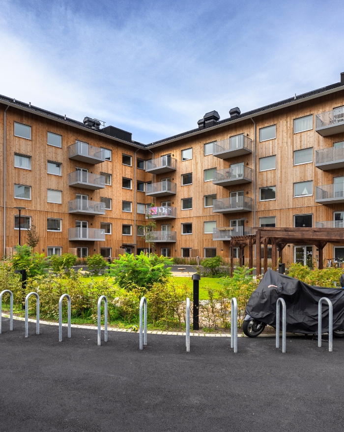 Bostadshus sett utifrån med träfasad och gröna buskar. Motorcykel står utanför.