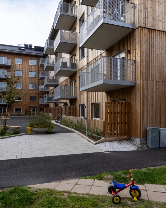 Bostadshus sett från sidan, med träfasad och balkonger. Barncykel står utanför