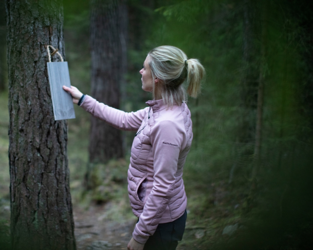 En kvinna i en skog som läser en skylt på ett träd