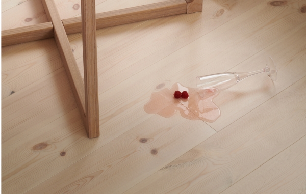 Ett ljust furugolv och ett utspillt champagneglas