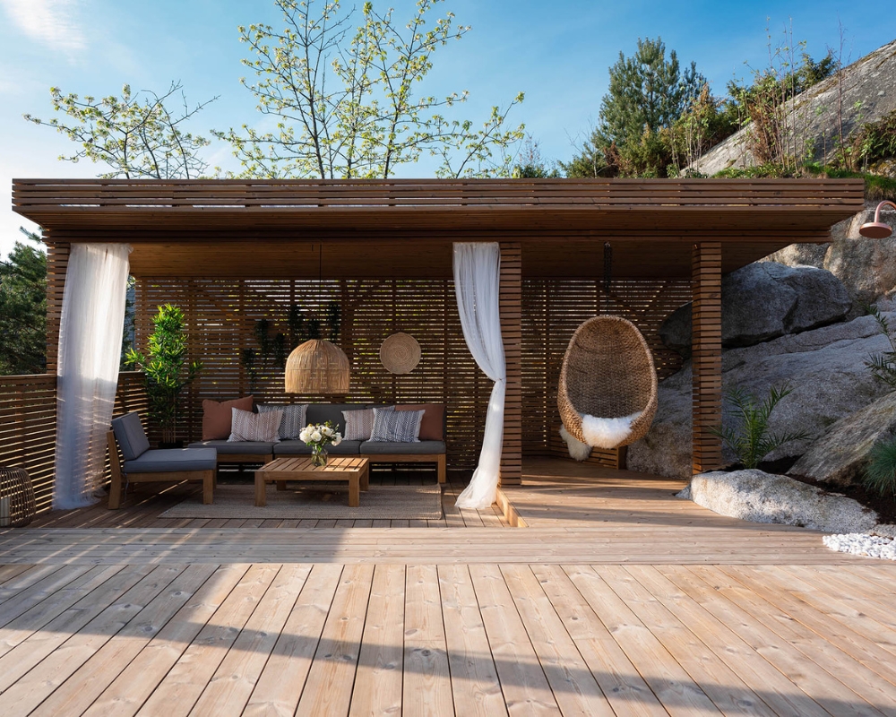 En altan med trall och utomhusmöbler, samt ett tak och staket byggt runt om i trä