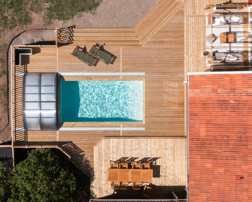 Ett foto ovanifrån ett hus med rött tak, altan med trall, pool och utemöbler