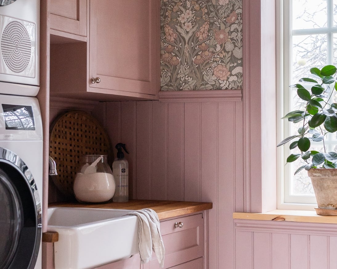 Tvättstuga med rosa bröstpanel, lister och skåp som matchar en blommig tapet.
