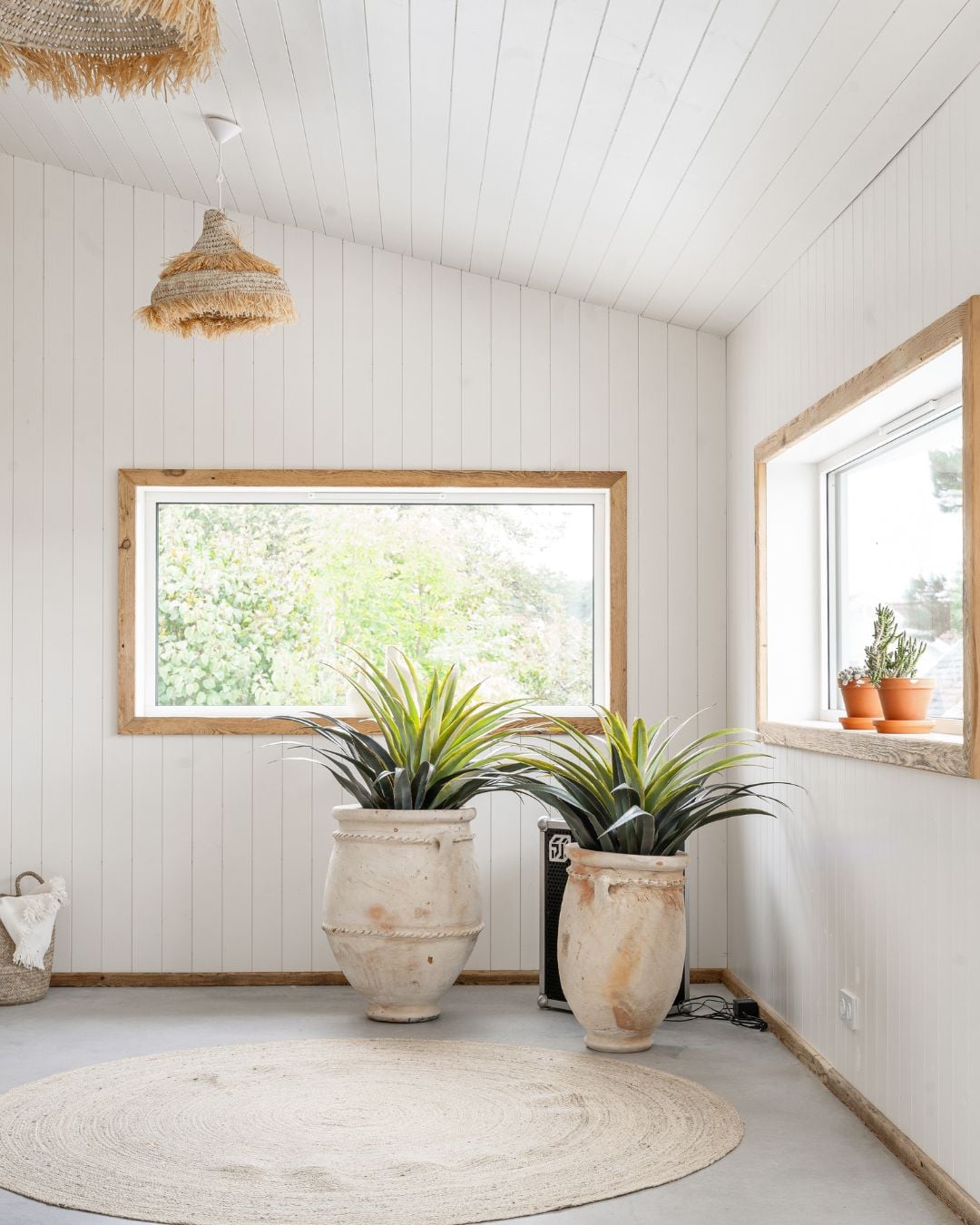 Hörnet på ett rum med stående vit träpanel Trend Slät, två fönster med foder av trä och två stora terrakottakrukor på golvet
