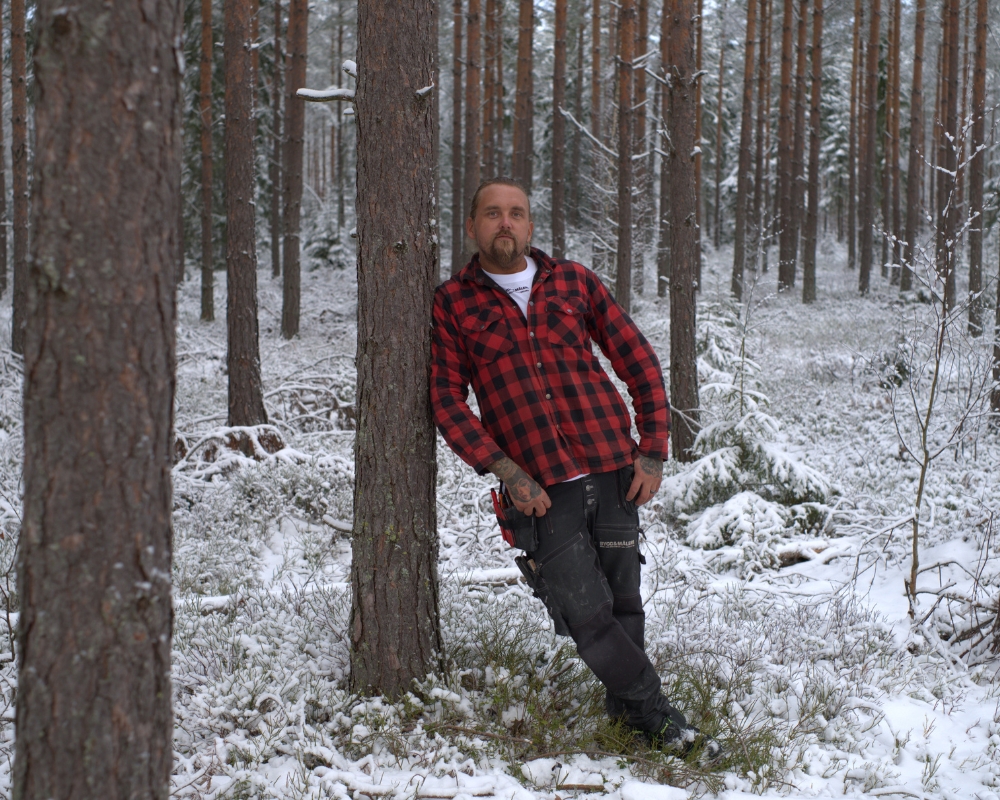En man i skogen som lutar sig mot ett träd, snö ligger på marken