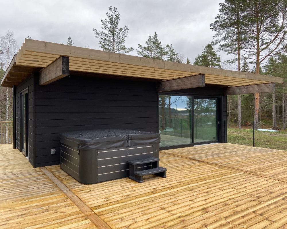 Ett svart hus med trätrall  och en jacuzzi
