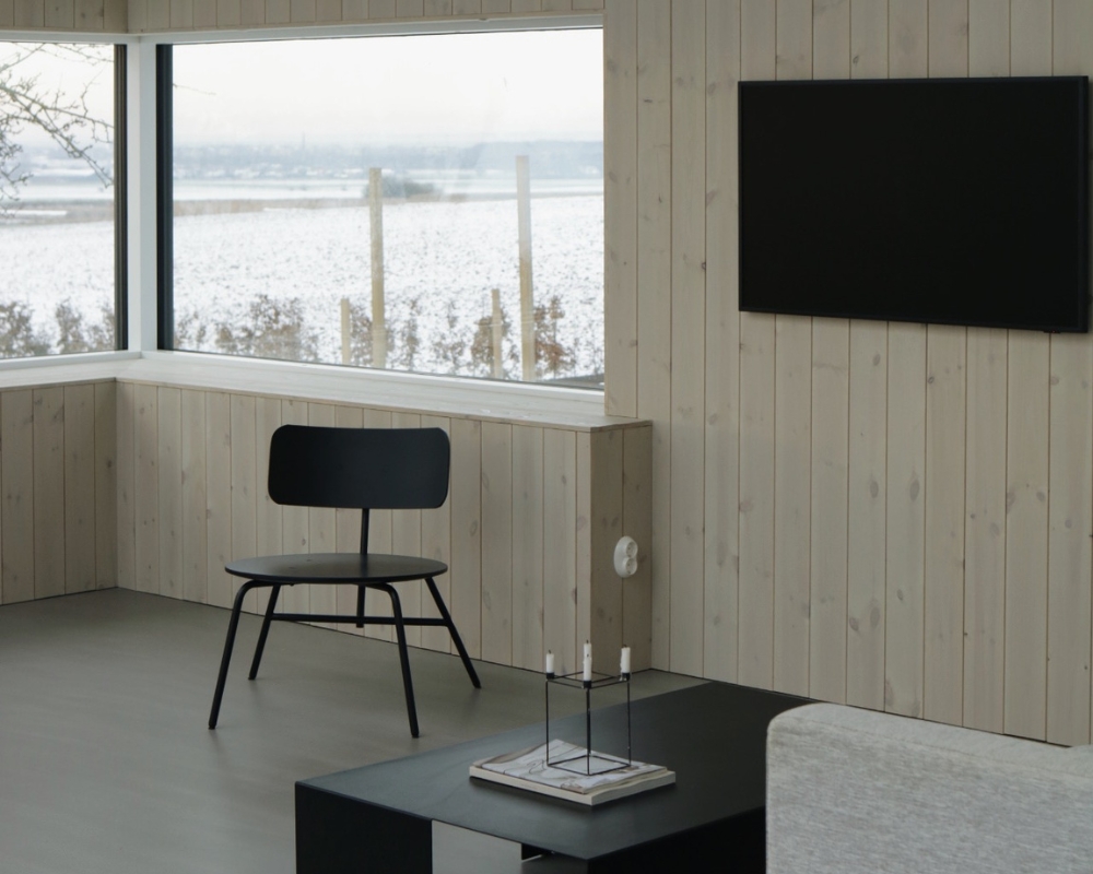 Fönster, en ljus innerpanel, tv på väggen, vardagsrumsbord, stol