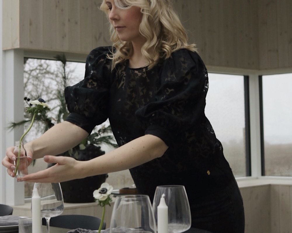 En kvinna, Johanna Sjölin, håller en liten vas med en blomma och dukar ett bord
