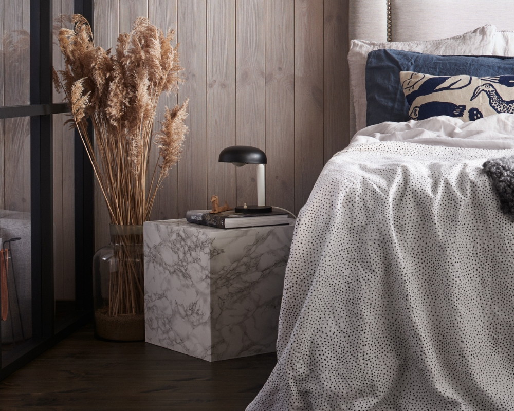 ett sovrum med en säng, sovbord, lampa, växt och en skiljevägg av svarta reglar