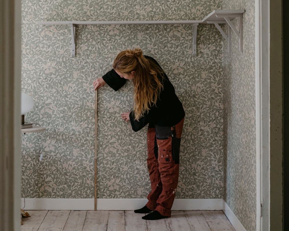 En kvinna mäter med en tumstock från golv upp på vägg