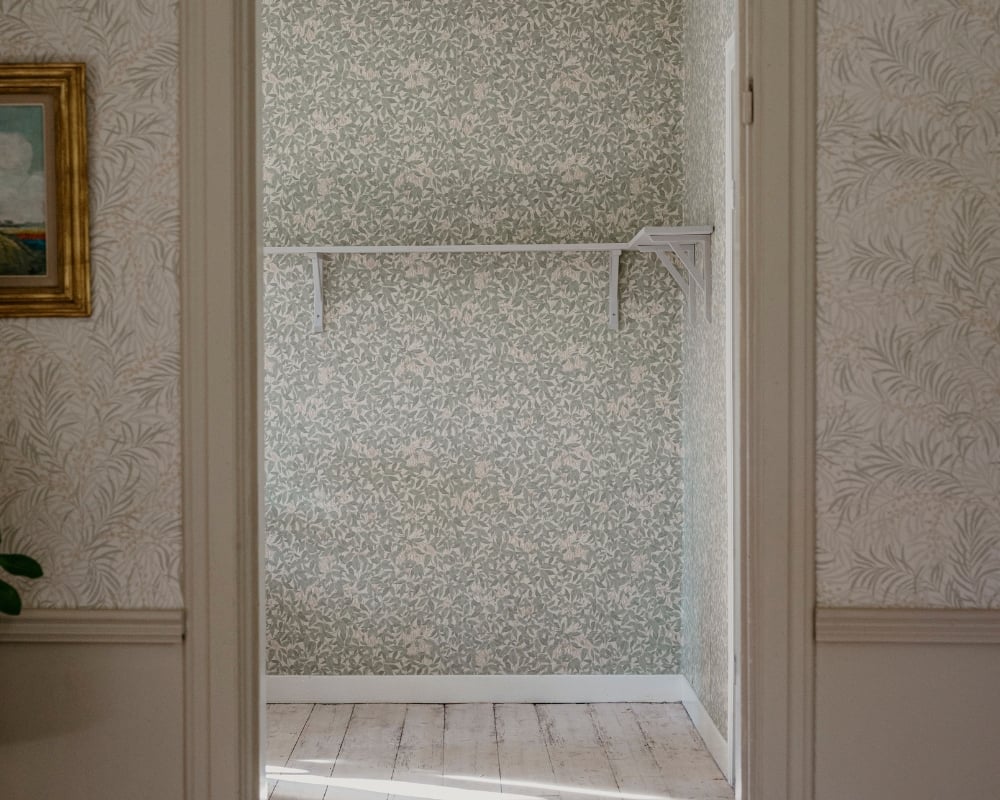 Öppning av en dörr, in till ett tomt rum med trägolv och tapet