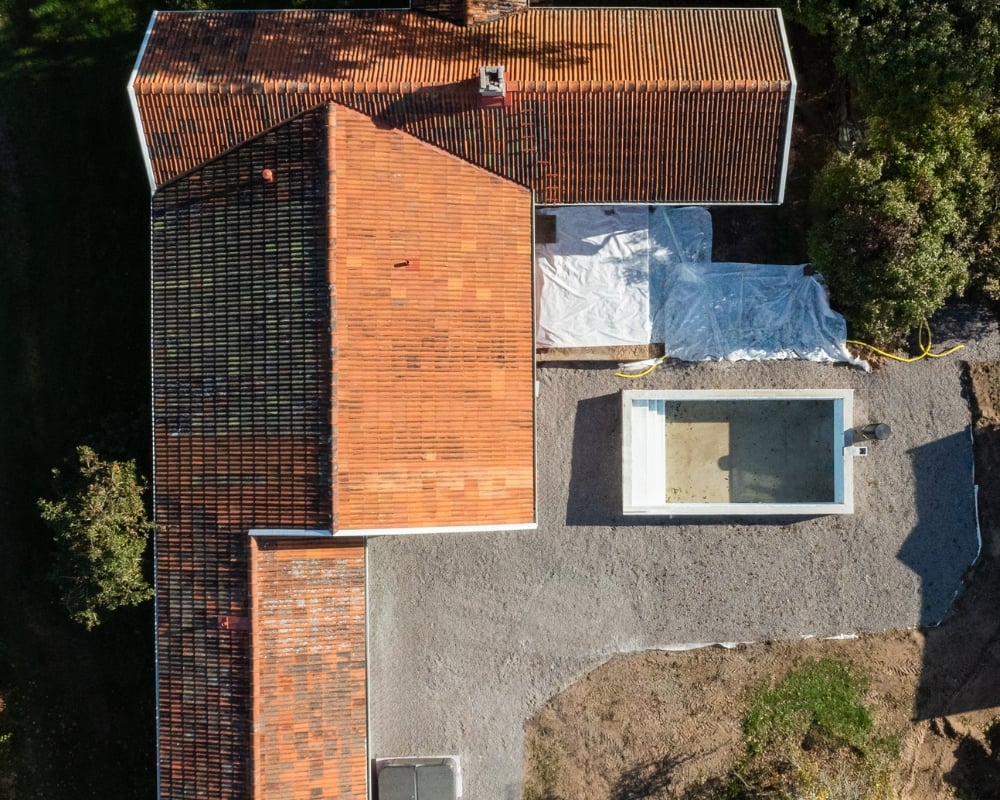 Foto taget ovanifrån ett hus med rött tegeltak, samt grunden för en pool