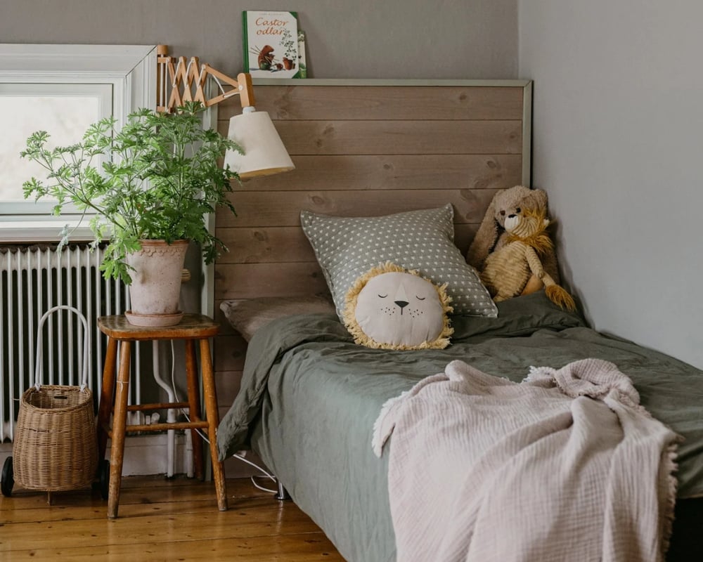 En säng med en sänggavel i trä, samt dekorationer i form av gosedjur, pall och växt 