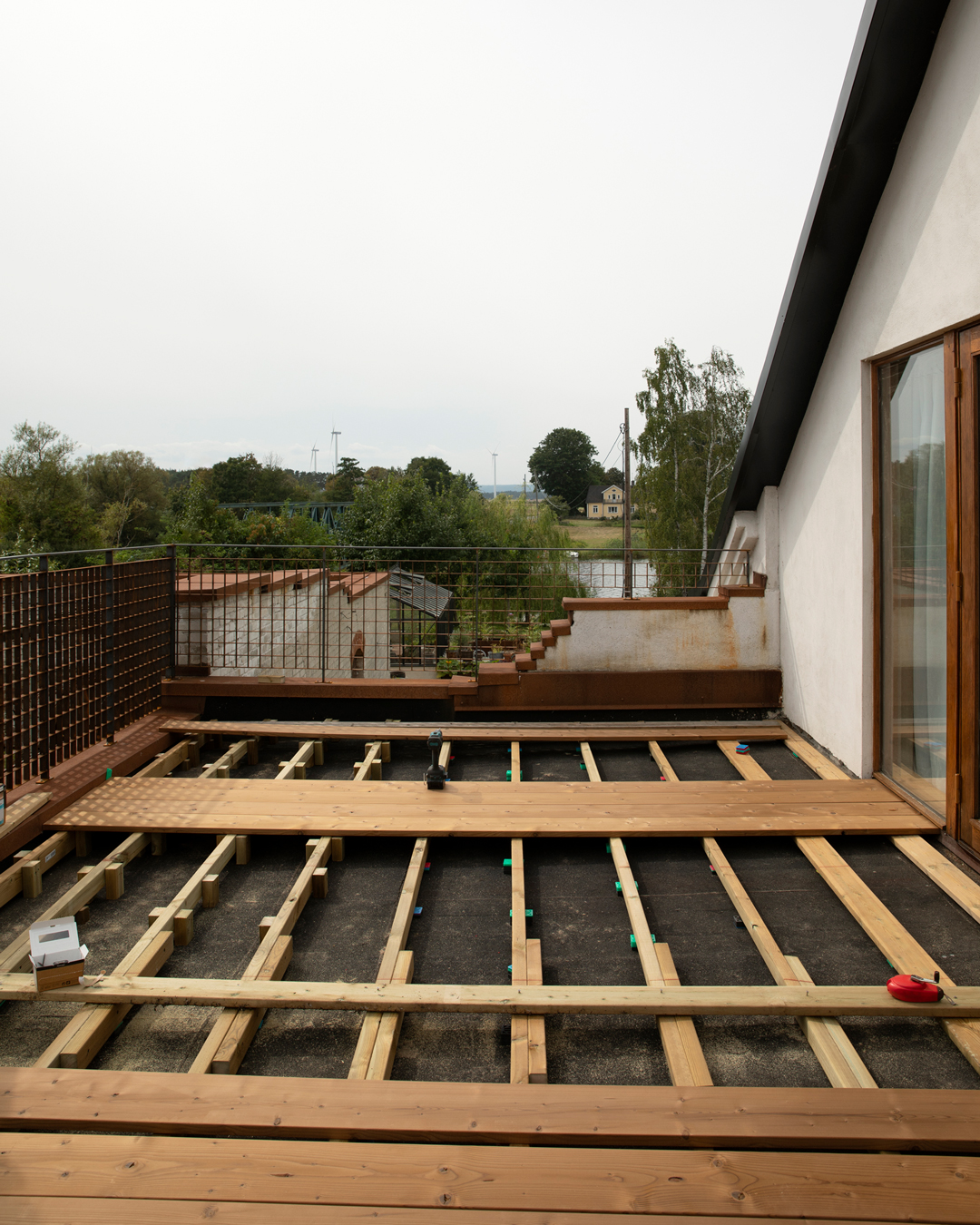 Regelverk byggt ovanpå takytan inför läggning av TermoGran-trall, med brädor och distanser utlagda och utsikt över fabriksområdet och landskapet i bakgrunden.