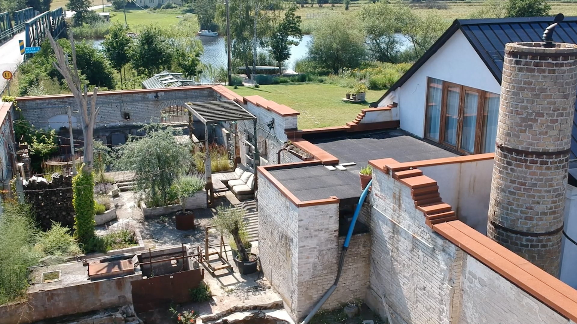 Översiktsbild över Stärkelsefabrikens innergård och den tidigare takytan innan terrassen byggdes, med murar, vegetation och vy mot ån i bakgrunden.