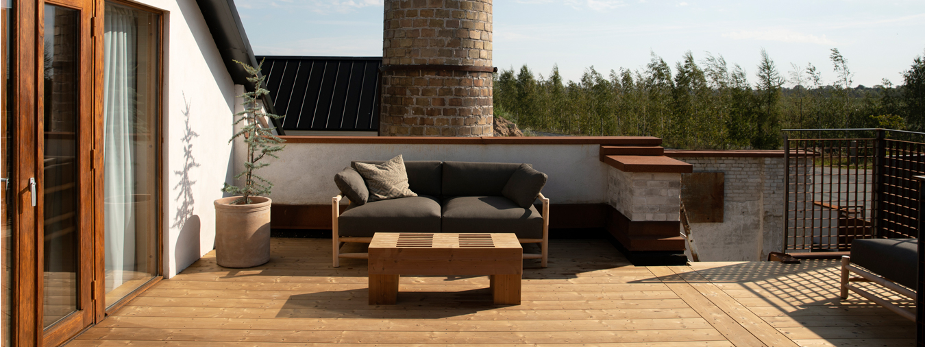 En person ligger och vilar på en träbänk framför en ljus tegelvägg, medan en hund ligger på gräset bredvid.