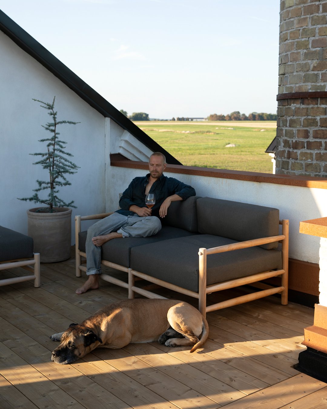 Gustav Ovland sitter i en utesoffa på takterrassen i kvällssol med ett glas i handen, medan hans hund ligger på TermoGran-trallen framför honom.