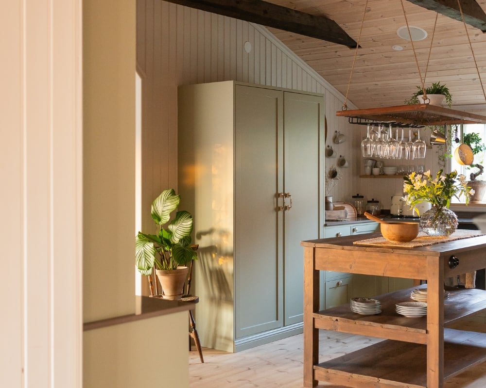 Ett kök med trä från golv till tak. En köksö i trä, ett grönt skåp och inredningsdetaljer